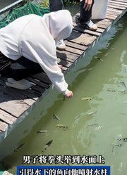男子将拳头举到水面上，引得水下的鱼向他喷射水柱